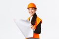 Pleased smiling female asian construction manager following blueprints during building house, looking satisfied at Royalty Free Stock Photo