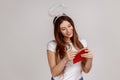 Pleased woman with nimbus over head holding red envelope, reading romantic letter with smile.