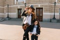 Pleased woman in white shirt with vintage camera walking around city with daughter and examines sights. Cute little girl Royalty Free Stock Photo