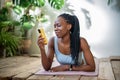 Pleased young african american woman lying on fitness mat with smartphone relaxing after training. Royalty Free Stock Photo