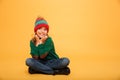 Pleased Young girl in sweater and hat sitting on floor Royalty Free Stock Photo