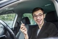 Pleased young man is holding the keys at his right hand while looking at the camera. He is sitting at his car Royalty Free Stock Photo