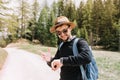 Pleased young man in sunglasses looking at wristwatch with smile standing on the road on nature background. Portrait of