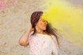 Pleased young model having fun in a cloud of yellow dry powder, celebrating Holi colors festival at the desert Royalty Free Stock Photo