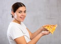 Pleased young woman holding piece of pizza