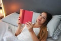 Pleased young woman reading a book lying in the bed the day off at home Royalty Free Stock Photo