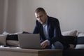 06.09.2022 - Pleven,Bulgaria - Young attractive man sitting on sofa at home working on laptop online, using internet, smiling, Royalty Free Stock Photo