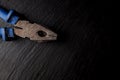 Pliers with a blue handle on a black stone background. Pliers, nippers isolated on black