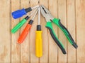 Pliers and four screwdrivers of different sizes with blue, green, red and yellow handles on a wooden table Royalty Free Stock Photo