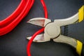 Pliers tool cutting red electric wire closeup on a black background Royalty Free Stock Photo