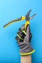 Pliers. Yellow and black pliers in the hand of an electrician on a blue monochrome background. Repair and installation tool. Royalty Free Stock Photo