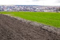Plowed agricultural field ready for seed sowing, planting process. Newly ploughed field with furrows, green grass. Sunny