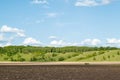 Plowed farm field with green hills, trees and blue sky in the background Royalty Free Stock Photo