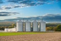 plowed field with silver silos and a farmhouse at the horizon