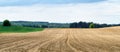 Plowed field  in spring in hilly terrain with forest in background. Blue sky and white clouds above. Royalty Free Stock Photo