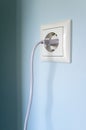 Plug with cable cord connected to the socket, on a blue wall. Royalty Free Stock Photo