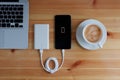 Plug in USB charger from powerbank input mobile phone or smartphone and laptop computer and coffee cup cappuccino on wooden floor, Royalty Free Stock Photo