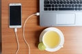 Plug in USB cord charger of the mobile phone with a laptop computer and freshly Lime juice in a white cup, on wooden floor Royalty Free Stock Photo