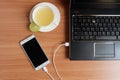 Plug in USB cord charger of the mobile phone with a laptop and freshly Lime juice in a white cup, on wooden floor Royalty Free Stock Photo