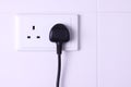 Plugged in socket against white tiles background