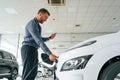 Plugging the charger. Handsome car dealership worker is with electric vehicle