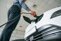 Plugging the charger. Handsome car dealership worker is with electric vehicle