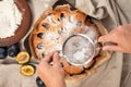 Plum torte decoration with icing. Hands holding sieve with sugar powder above plum pie. Making fruit pie bakery. Royalty Free Stock Photo