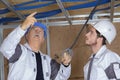 Plumber and apprentice holding blue pipe above ceiling