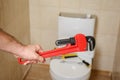 Plumber holding pipe wrench near toilet indoors, Royalty Free Stock Photo