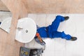 Plumber Lying On Floor Repairing Sink In Bathroom Royalty Free Stock Photo