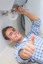 Plumber repairing washbasin drain while gesturing thumbs up