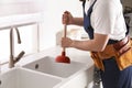 Plumber using plunger to unclog sink drain in kitchen, closeup Royalty Free Stock Photo