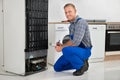 Plumber Writing On Clipboard In Front Of Refrigerator