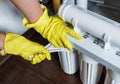 Plumber in yellow household gloves changes water filters. Repairman installing water filter cartridges in kitchen. Drinkable water