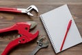 Plumbing tools, notebook with blank page and red pencil, on brown wooden background. Flat lay, top view, copy space. Fix list Royalty Free Stock Photo