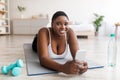 Plump black woman with bottle of water and smartphone browsing internet, checking social network at home