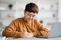 Plump chinese boy nerd doing homework, using laptop