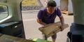 Caucasian man unloads wooden planks from car trunk to station of collection of large-size garbage on spring sunny day