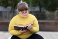 Plump girl in glasses sits alone in park and reading book