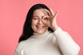 Plump Girl Looking Through Ok Sign Gesture, Posing Over Pink Background