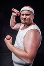 A plump man works out with two small dumbbells. The background is black