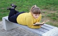 Plump satisfied girl lies on park bench alone and reads book