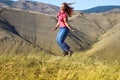 Plump white haired caucasian girl in jeans and hiking boots jumping on the field