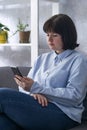 Plump young woman in jeans and formal shirt looks into phone. Girl in reception is sitting on couch