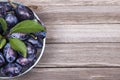 Plums with green leaves in a bowl on wooden background. Top view. Royalty Free Stock Photo