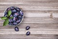 Plums with green leaves in a bowl on wooden background. Top view. Royalty Free Stock Photo