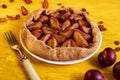 Plums pie with raisins on a white plate on yellow wooden background decorated with three fresh plums, brown raisins Royalty Free Stock Photo