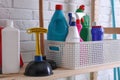 Plungers and basket with detergents on wooden shelf near white brick wall Royalty Free Stock Photo