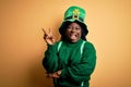 Plus size african american woman with braids wearing green hat with clover on st patricks day smiling with happy face winking at