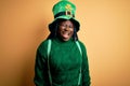 Plus size african american woman with braids wearing green hat with clover on st patricks day winking looking at the camera with